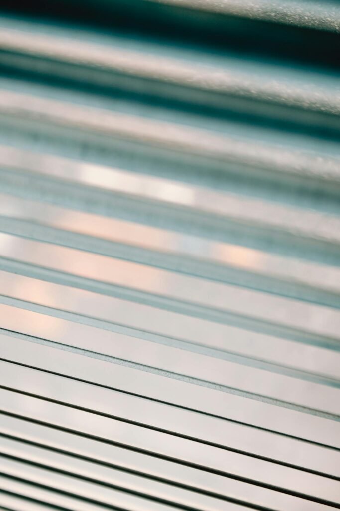 Closeup of half closed white metal blinds covering window in apartment during day